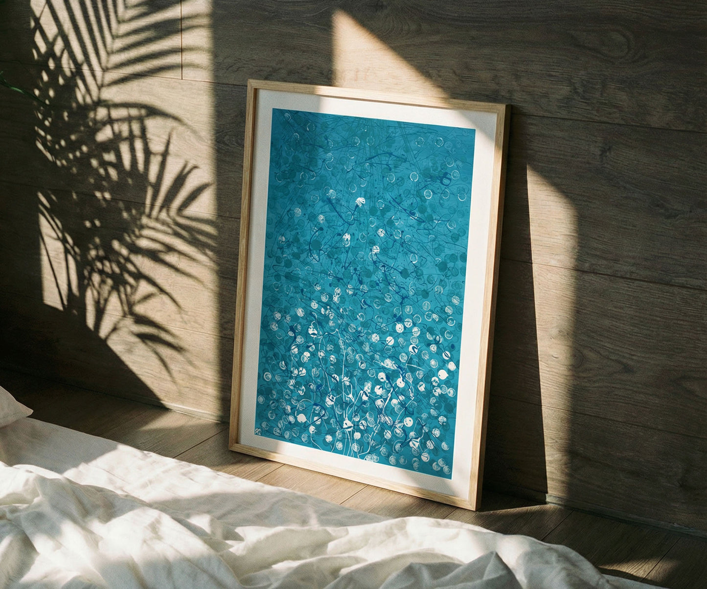 Framed blue abstract artwork leaning against a wall with sunlight casting plant shadows.