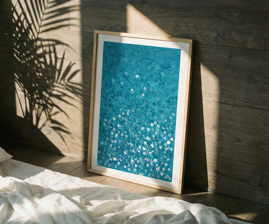 Framed blue abstract artwork leaning against a wall with sunlight casting plant shadows.