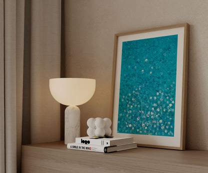 Framed blue abstract artwork displayed on a wooden cabinet beside a table lamp.