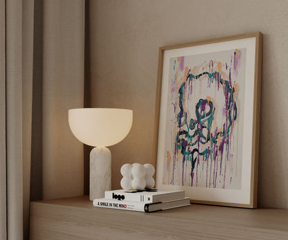 Framed abstract skull art print by The Jana Saga styled on a wooden cabinet beside a lamp.