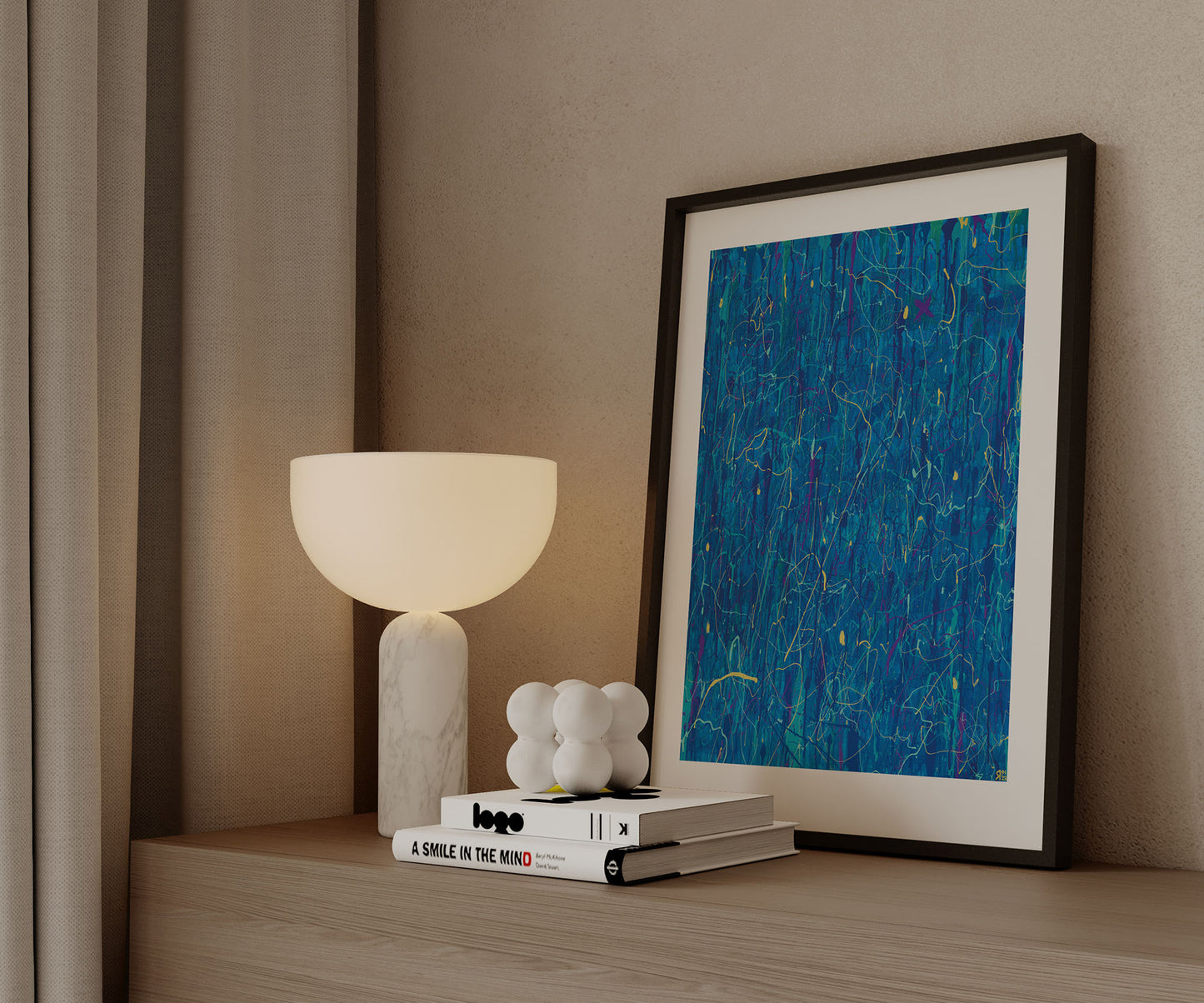 Framed blue abstract wall art print by The Jana Saga styled on a wooden cabinet beside a modern table lamp.